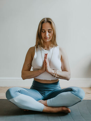 Woman sitting cross-legged on a mat with hands together.