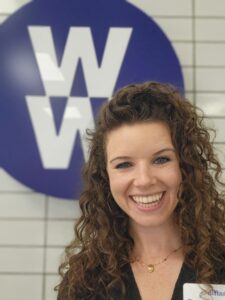 Website owner smiling indoors in front of a wall sign.