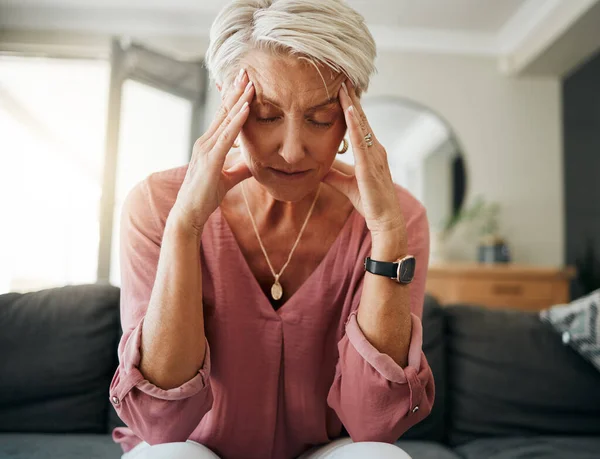 Woman sitting on a couch holding her head, appearing stressed.